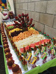 an assortment of fruits and vegetables displayed on a table with people in the background looking at them