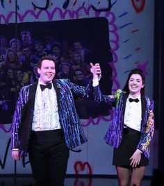 two people in tuxedos on stage with one holding up the other's hand