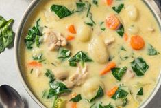 a bowl filled with chicken and spinach soup next to a spoon on top of a table