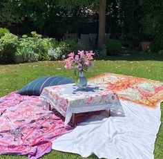 two blankets and a vase with flowers on the ground in front of some trees,