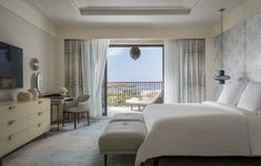 a bedroom with a bed, dresser and television in front of a balcony overlooking the ocean