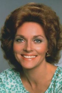 a woman with brown hair and blue eyes smiles at the camera while wearing a green shirt