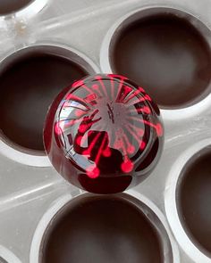 a red and black object sitting on top of a muffin tin filled with chocolate