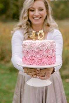 a woman holding a pink cake with the number forty on it in front of her