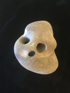 a white mask with holes in the middle on a black background, it appears to have been made out of clay