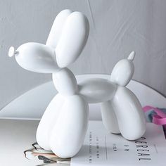 a white balloon dog sitting on top of a book next to a pink streamer