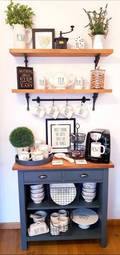 a coffee bar with cups and plates on the shelf above it is decorated with greenery