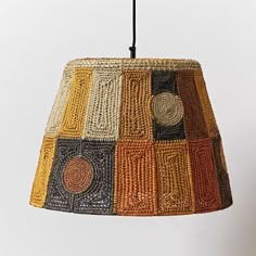 a multicolored lamp shade hanging from a black cord on a white wall background