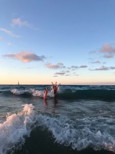 two people standing in the ocean with their arms up