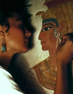 two women are kissing each other in front of an egyptian wall painting with gold and blue accents