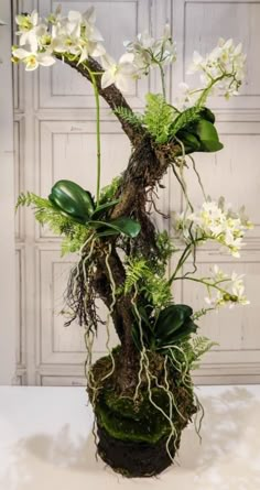 an arrangement of white flowers and greenery in a mossy vase on a table