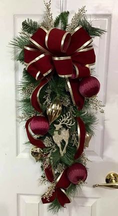 a christmas wreath hanging on the front door with red and gold ribbons, ornaments and bells