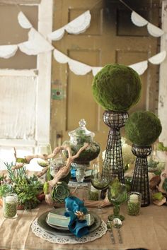 a table topped with lots of green plants and vases filled with flowers on top of a wooden table