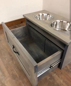 an open drawer with two bowls in it on the floor next to a dog bowl