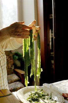 a person holding up some green vegetables on top of a white plate in front of a window