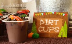 dirt cups are sitting on the floor next to a sign and some candies in a cup