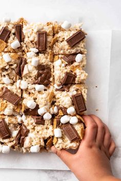 someone is holding up a chocolate and marshmallow snack bar on a sheet of parchment paper