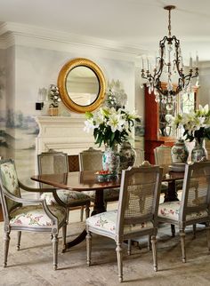 a formal dining room table and chairs with floral upholstered cushions, in front of a fireplace