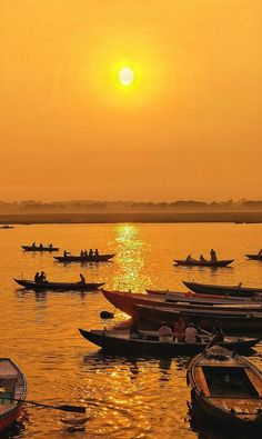 many small boats floating in the water with people on them at sunset or sunrise time