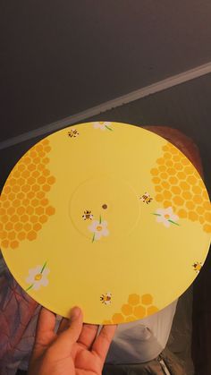 a person holding up a yellow plate with flowers on it and bees around the edges