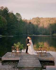 a bride and groom kissing on a dock in front of a lake surrounded by chairs