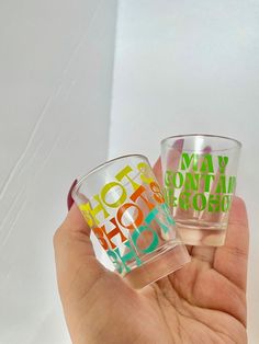 two shot glasses with different colored letters on them in the palm of someone's hand