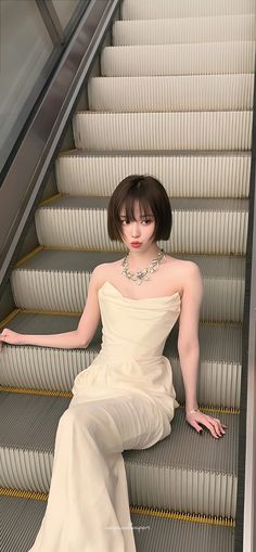 a woman sitting on an escalator wearing a white dress