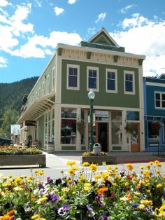 a green building with flowers in front of it and mountains in the backround