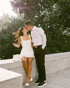 a man and woman are kissing on the wall with trees in the backgroud