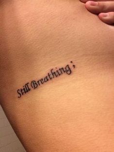 a woman's stomach with the words still breathing tattooed on her lower back side