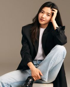 a woman sitting on top of a white stool wearing jeans and a black blazer