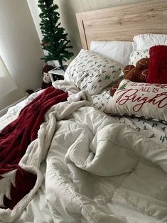 an unmade bed with pillows and blankets on top of it, next to a christmas tree