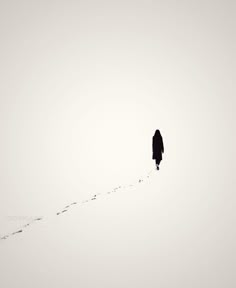 a person walking across a snow covered field with a kite in the sky behind them