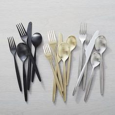 five different types of forks and spoons lined up on a white surface with one black fork, the other gold