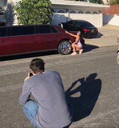 a man taking a photo of a woman in front of a red car with her shadow on the ground