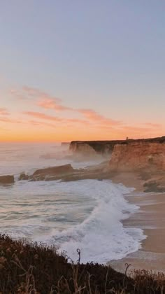 an ocean view with waves crashing on the shore and cliffs in the background at sunset