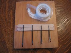 a pair of scissors and tape are on a wooden board next to some sewing needles