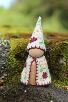 a small knitted christmas tree decoration sitting on top of a moss covered rock wall