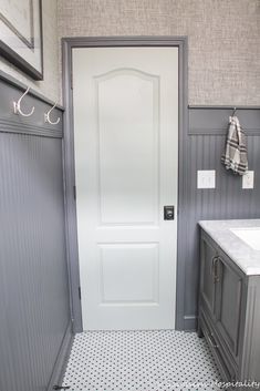 a white door in a gray bathroom with black and white floor tiles on the walls