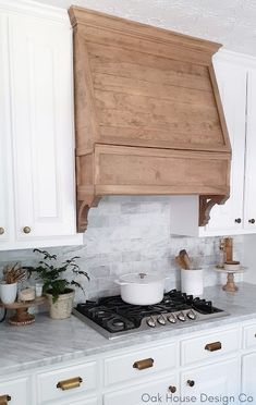 a kitchen with white cabinets and wooden hood over the stove top, surrounded by potted plants