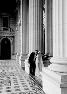 a bride and groom standing in front of columns