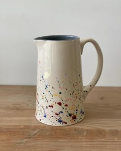 a white coffee mug with multicolored splatters on it sitting on a wooden table