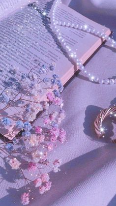 an open book on a table with flowers and pearls next to it, surrounded by jewelry