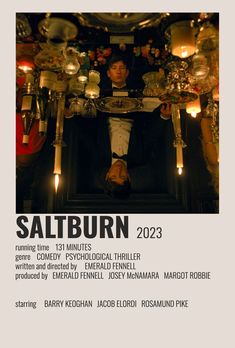 a man sitting in a chair with candles on the table behind him and an advertisement for saltburn