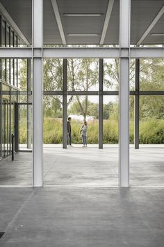 two people standing in an open space with large windows on each side and trees behind them