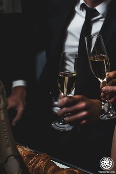 black and white photograph of two people holding wine glasses in front of each other,