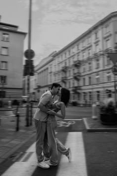 a man and woman kissing on the street with buildings in the backgrouds