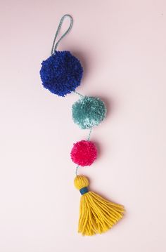 three pom - poms hanging from a string on a pink background with copy space