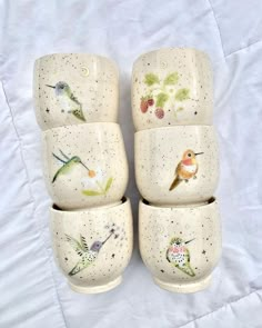 four ceramic cups with birds painted on them sitting on a white cloth covered tablecloth