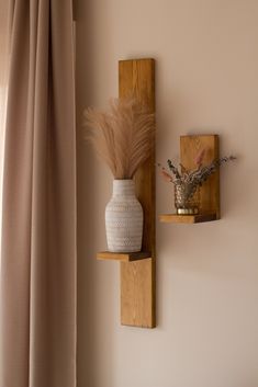 two wooden shelves with vases and plants on them in front of a beige curtain